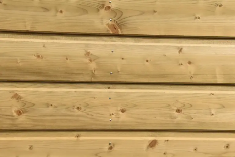 Close-up of light-colored wooden wall planks with visible knots and nails, typical construction lumber used for garage shelves.