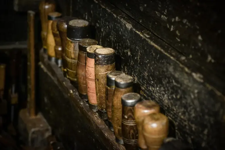 Row of wooden-handled chisels standing upright in a dusty, dimly lit workshop shelf