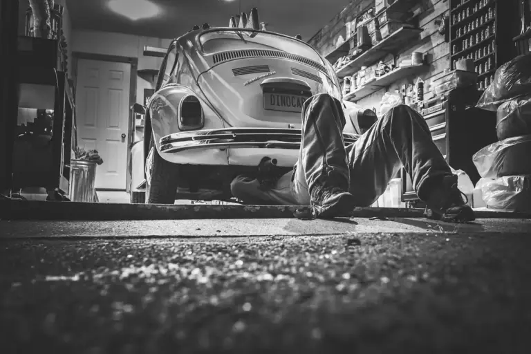 Person lying on the garage floor under a car, working in a cluttered home workshop