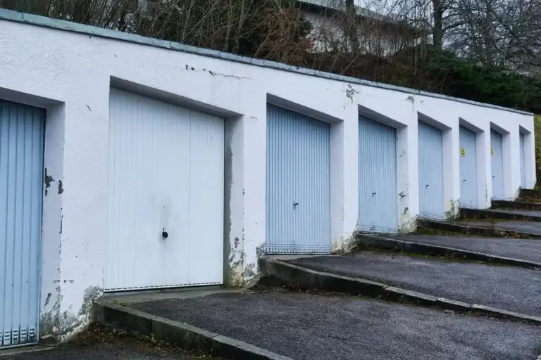 Row of white garage doors along a sloped concrete driveway with steps to the side