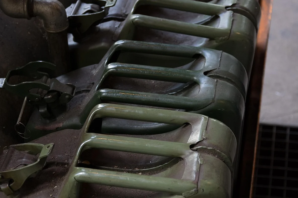 Several green plastic gasoline containers (jerry cans) stacked and stored in a garage or utility area.