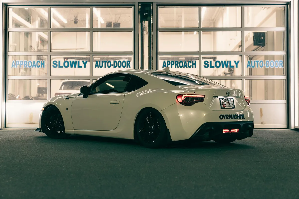 White sports car parked in front of a garage with auto-door panels labeled 'Approach Slowly', illustrating a workspace where a gearhead might install a garage door opener.