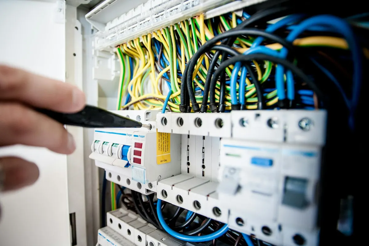 Close-up of an electrical panel with many colored wires and a hand using a screwdriver near the breakers.