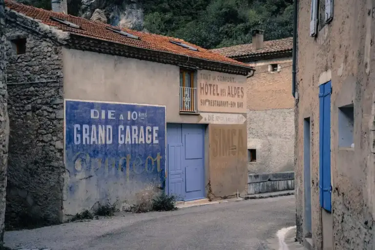 A narrow street with weathered buildings; a large blue sign reading 'GRAND GARAGE' on one wall