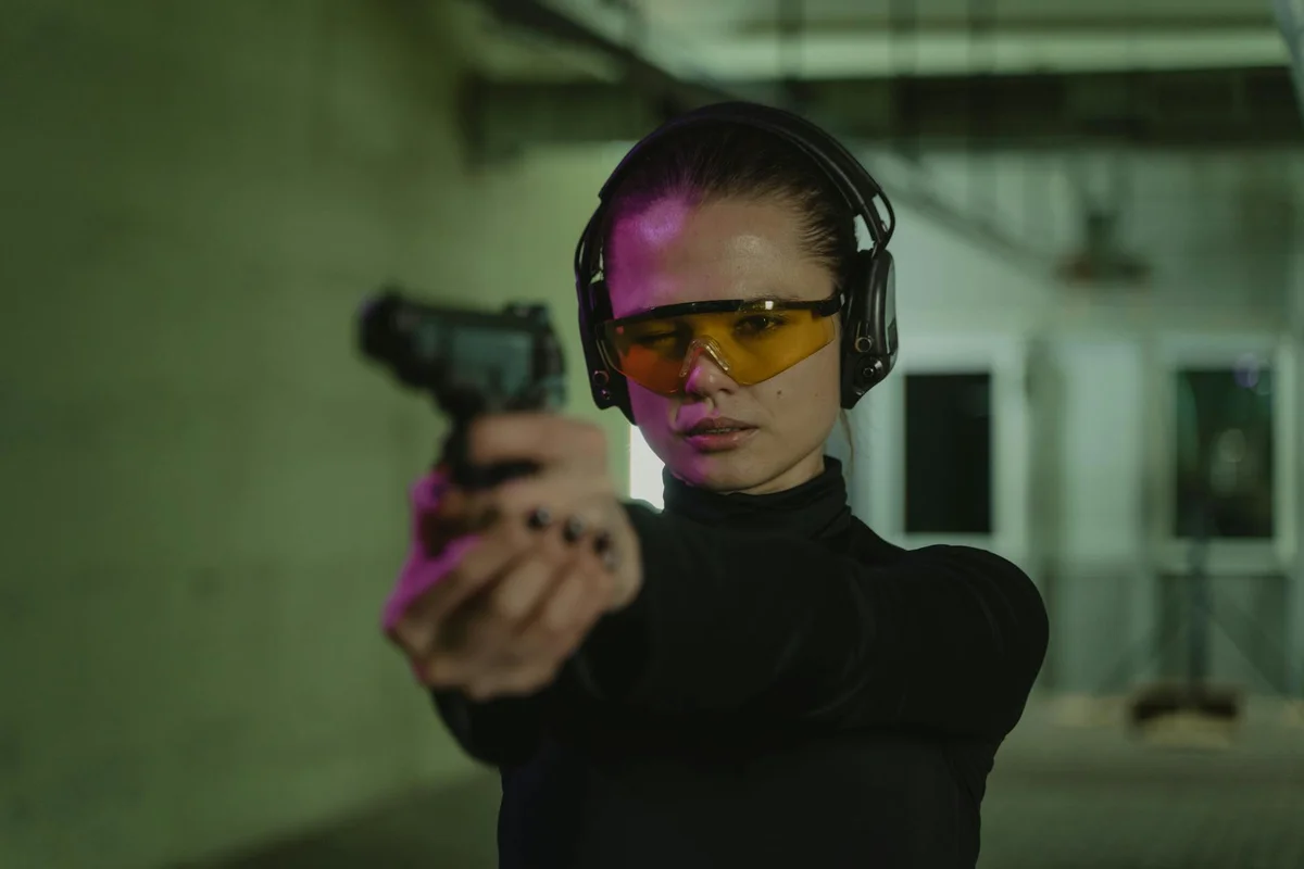 Person wearing safety glasses and hearing protection, holding a handgun at an indoor range.