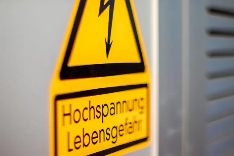 Yellow high voltage warning sign with a black lightning bolt and German text Hochspannung Lebensgefahr beside electrical panel