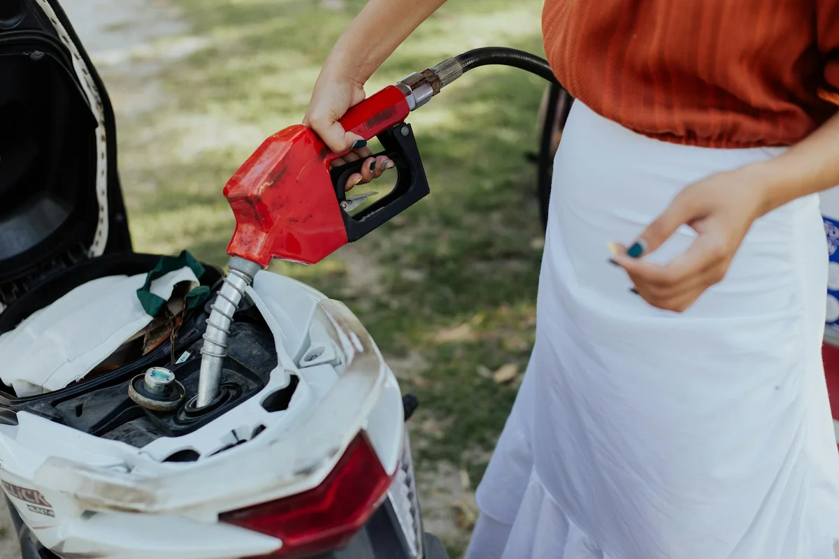 Person near an open trunk handling gasoline with a pump nozzle nearby, illustrating gasoline handling in the context of home garage safety.