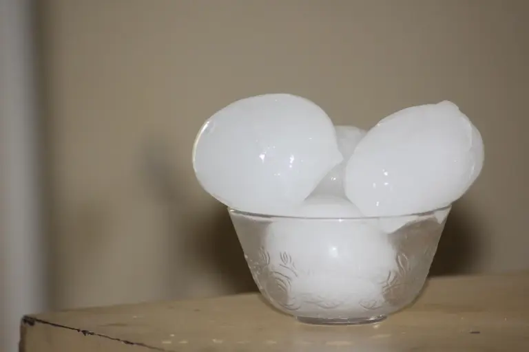 A glass bowl filled with large ice cubes resting on a wooden surface
