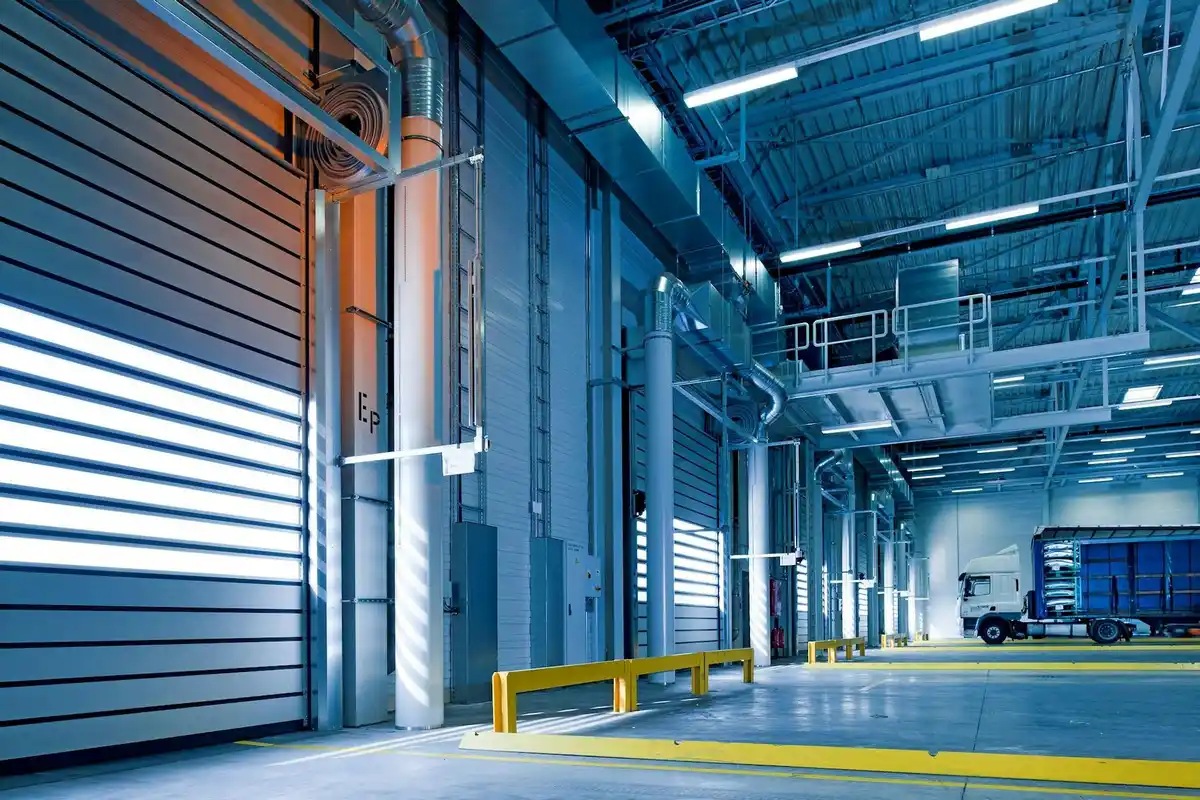Industrial warehouse interior with blue epoxy-coated concrete floors, yellow safety barriers, and bright overhead lighting.