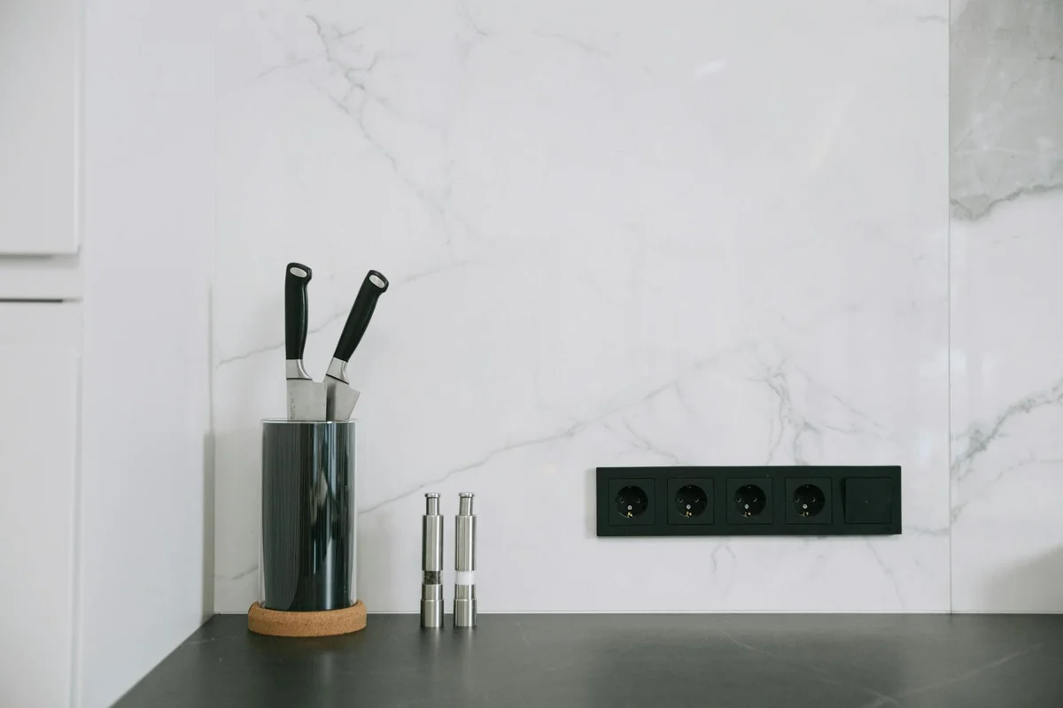 Kitchen counter with a knife block and a black wall outlet strip on a white marble backsplash.