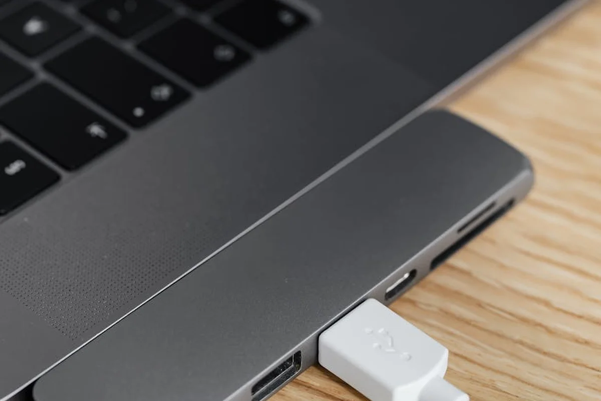 Close-up of a laptop with a white USB-C Ethernet adapter plugged in on a wooden desk.