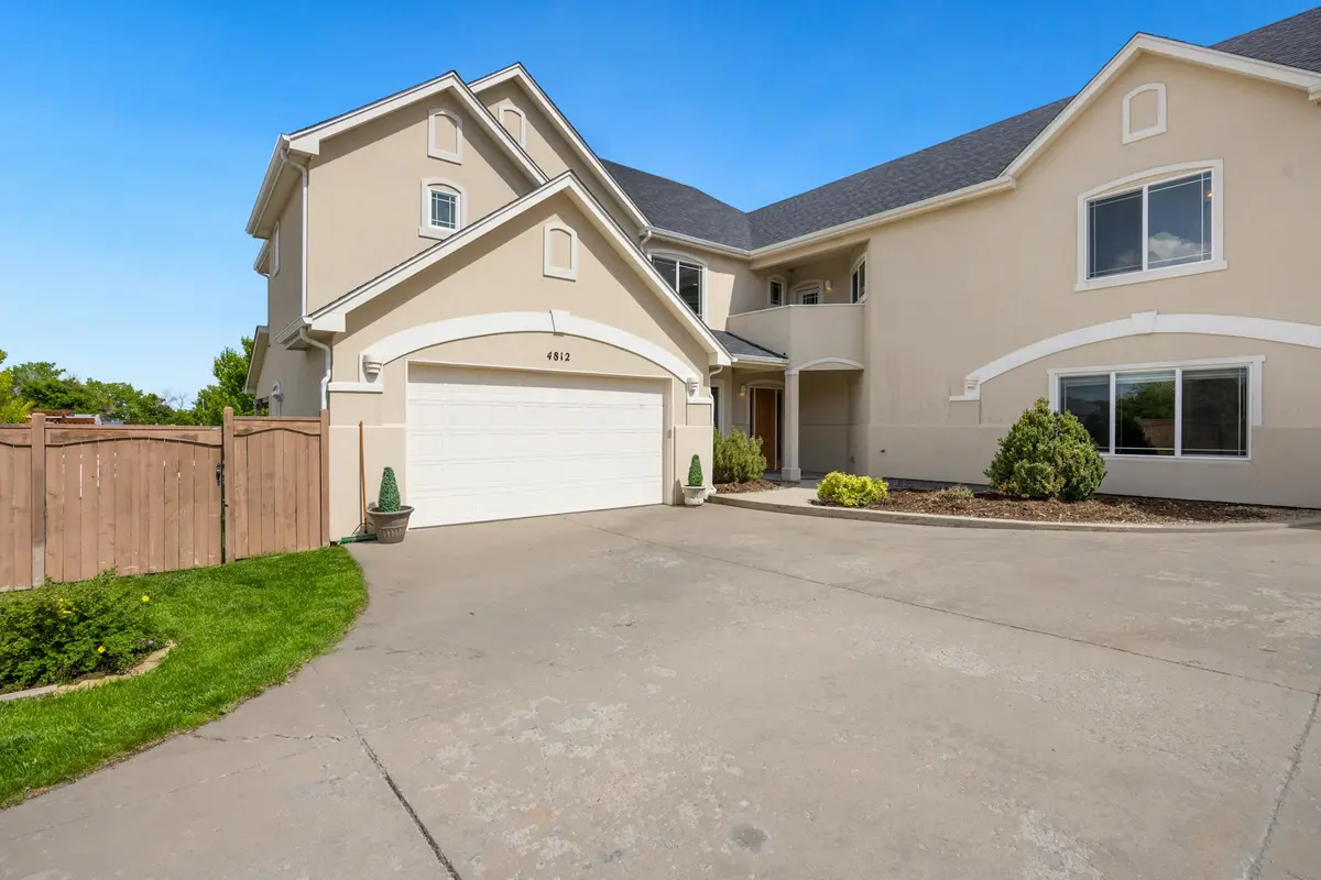 Modern beige suburban house with a two-car garage and a clean, wide driveway under a clear blue sky.