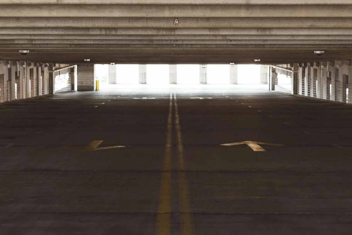 Interior view of a dark parking garage with concrete ceiling and columns; a long open lane toward a bright exit, illustrating overhead space above a doorway suitable for storage.