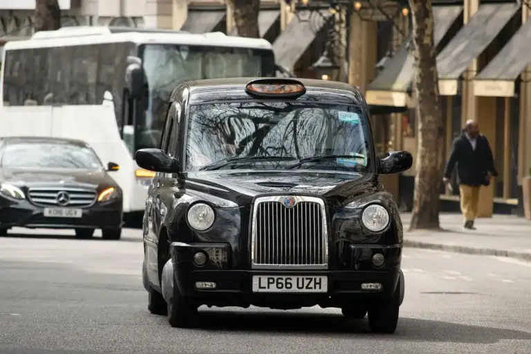 A black London taxi driving down a city street.