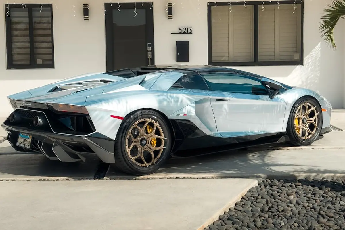 A silver-blue luxury sports car parked in a residential driveway in front of a modern house.
