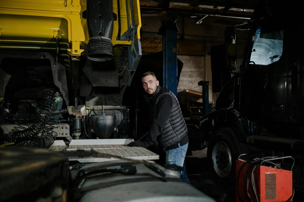 Person in a dark jacket examining mirrors and sightlines beside a large vehicle in a workshop, preparing for parking in a narrow garage.