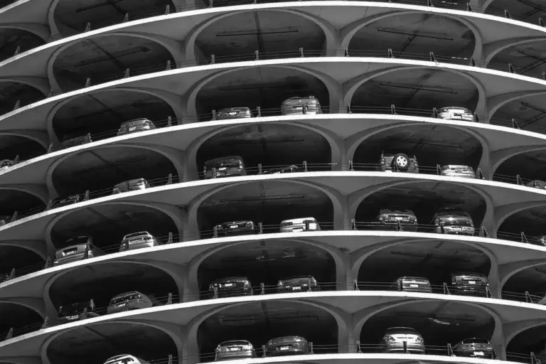 Black-and-white photograph of a multi-level circular parking garage with cars parked on each level, showing curved ramps and stacked parking.