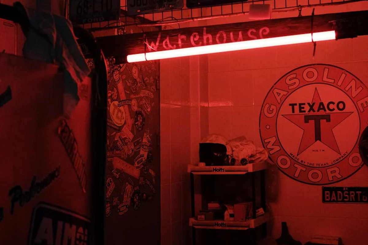 Dimly lit garage corner with red neon lighting, vintage signage, and compact wall-mounted shelving for organized storage.