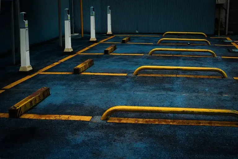 A narrow parking area with yellow bumper rails and parking blocks on a blue concrete floor, showing limited space between walls.