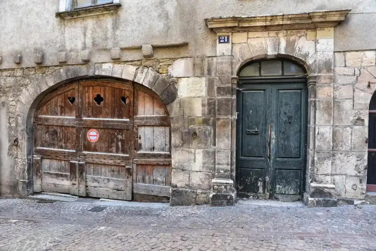 Two large doors set into a weathered stone building along a cobblestone street, resembling a garage entrance.