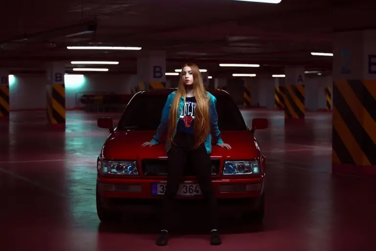 A person standing in front of a red car inside a dimly lit underground parking garage.