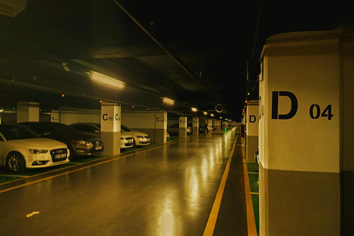 Nighttime parking garage with a glossy epoxy-coated concrete floor reflecting overhead lights; pillars line the aisles with cars parked along both sides.