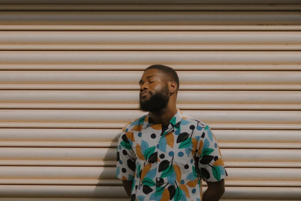 Man wearing a colorful leaf-pattern shirt stands against a beige garage door.