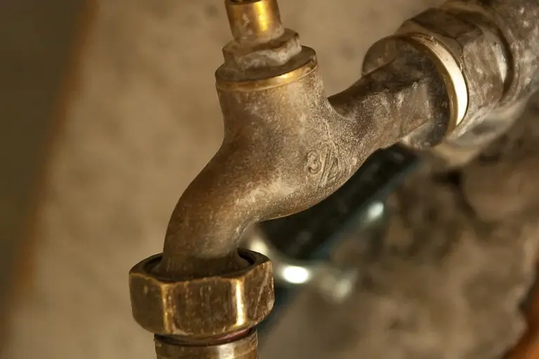 Rusty metal plumbing valve with connected pipes, showing joints and fittings in a garage or utility area.