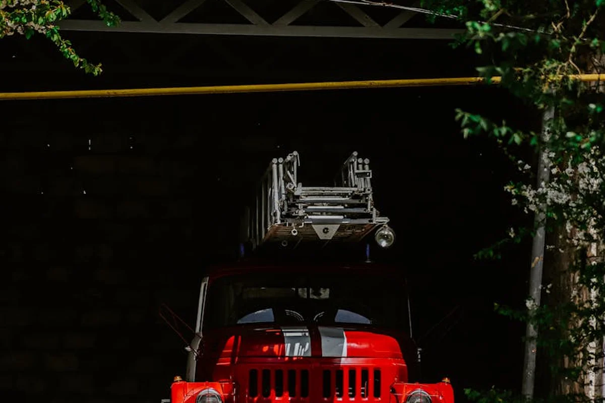 Red fire truck with a ladder on top parked in a dark garage or tunnel opening