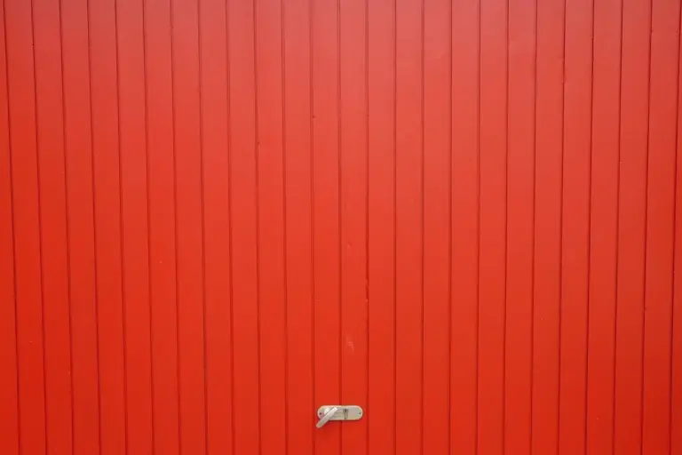 Close-up of a red garage door with a small metal manual release lever near the bottom center.