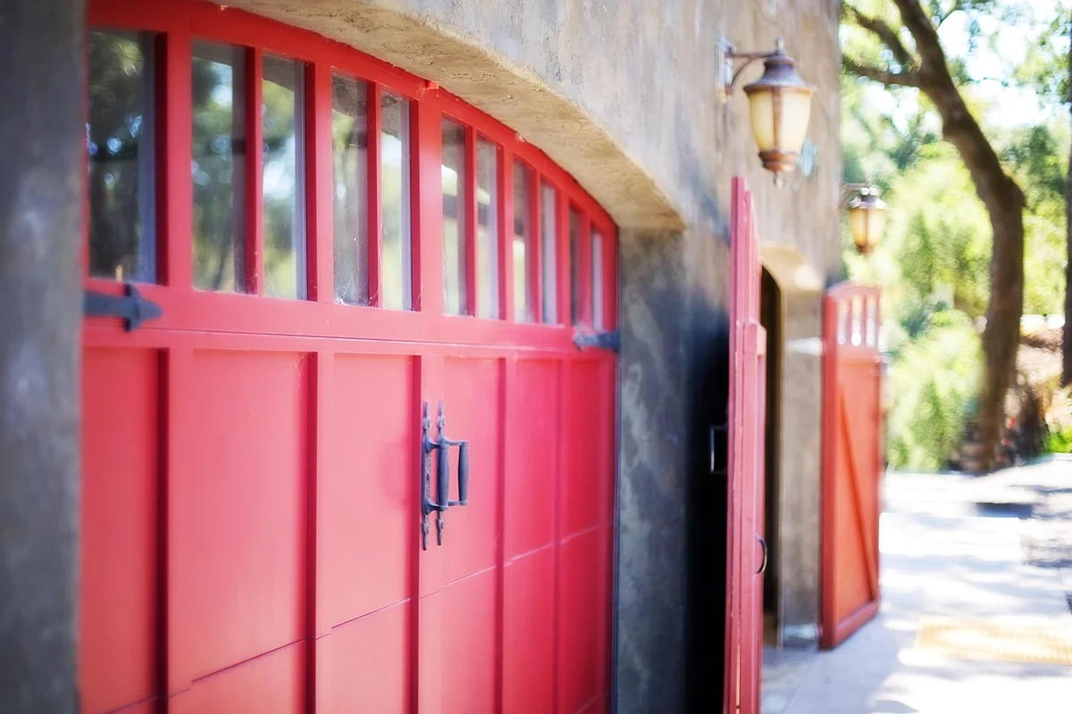 Red sectional garage door with windows along the top, mounted in a stucco exterior.