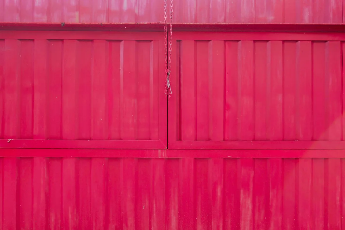 Red sectional garage door with a hanging chain in the center, showing a manual locking point.
