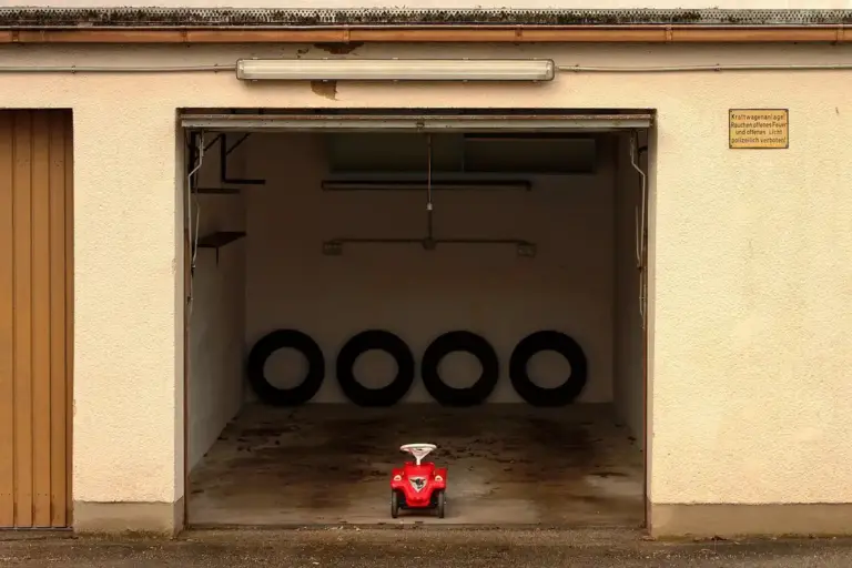 Open garage with a row of tires along the back wall and a small red toy car in the center, illustrating scale for RV garage door dimensions.