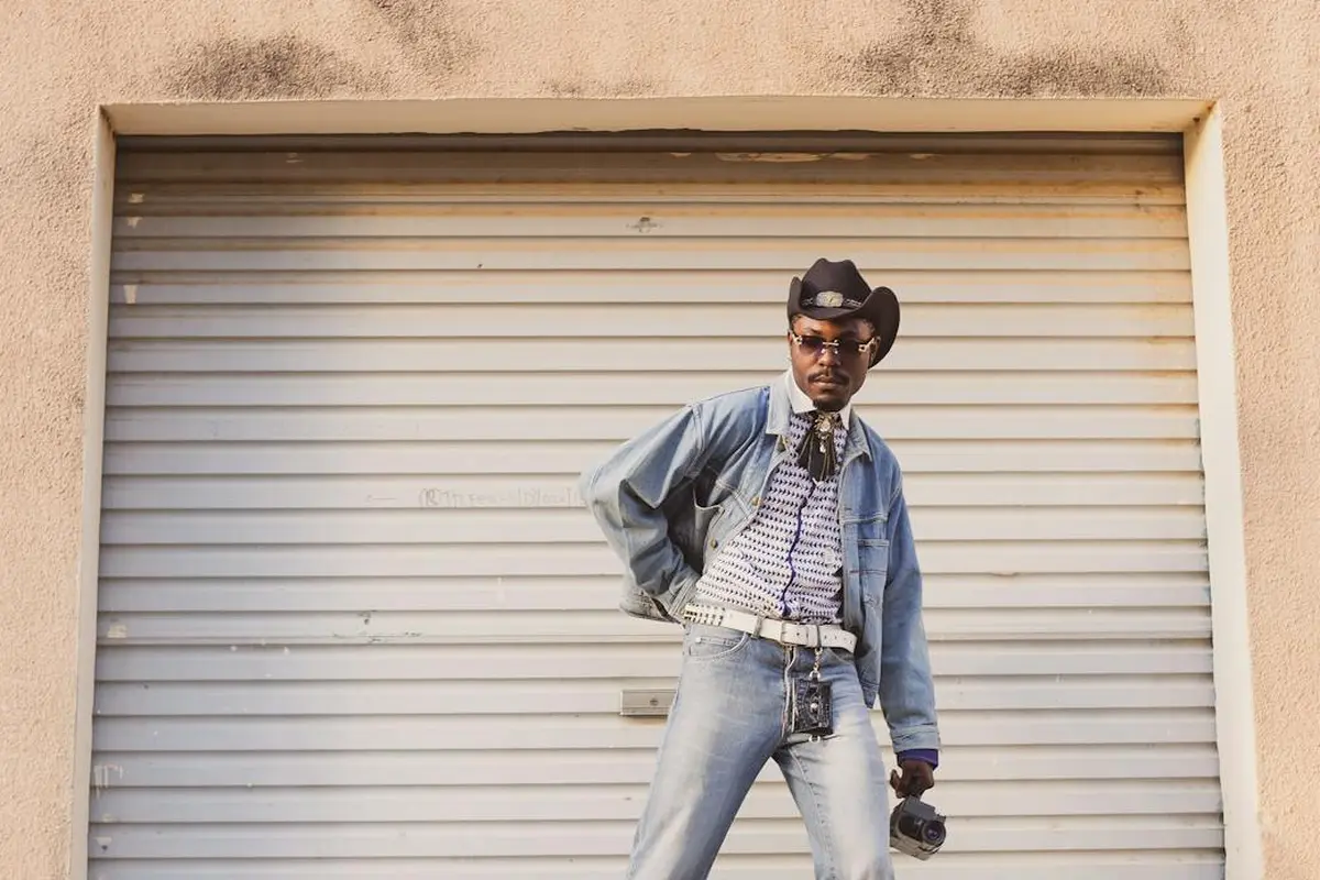 Person in denim outfit and cowboy hat standing in front of a closed metal garage door