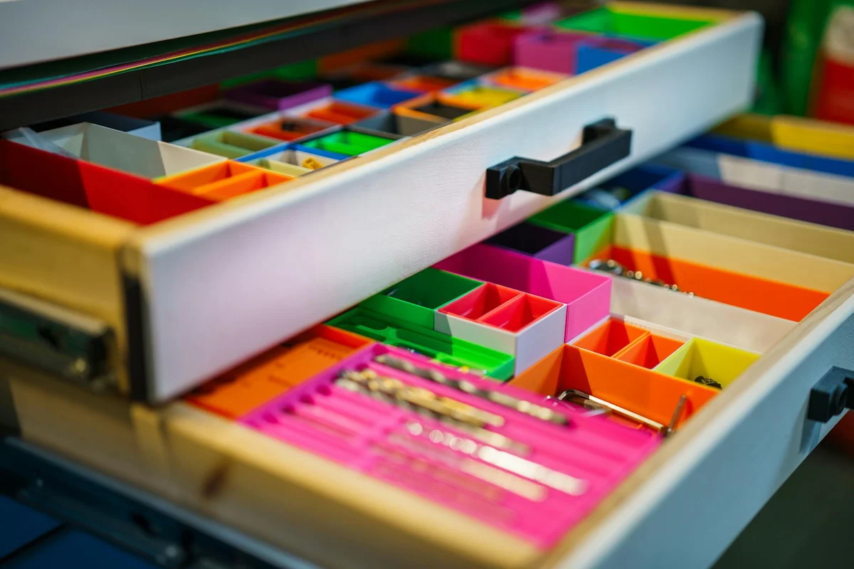 Close-up of a multi-drawer storage organizer with colorful dividers, used to sort small hobby parts in a garage workshop.