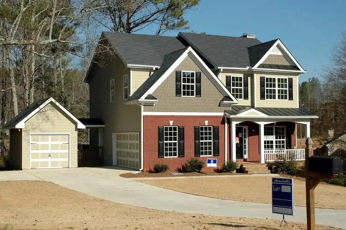 Two-story suburban home with an attached two-car garage, a small detached outbuilding on the left, and a front yard with a for-sale sign.