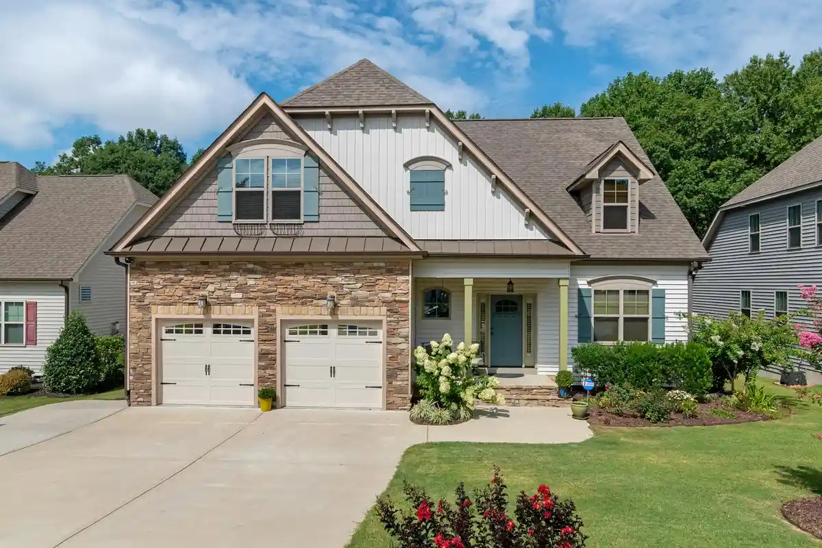 A sunny suburban house with a two-car garage, stone accents, and a well-kept lawn