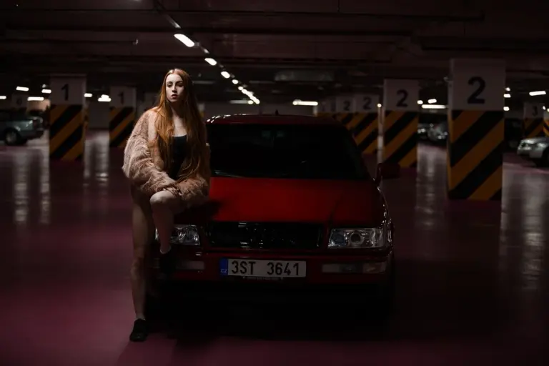 A person leaning on a red car in an indoor parking garage