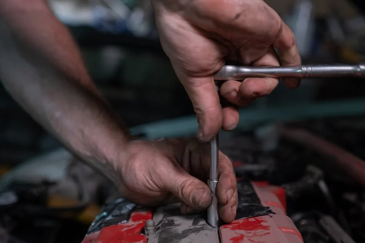 Close-up of hands using a wrench-like tool on a red work surface in a busy workshop, illustrating a hands-on approach for visualizing space in a garage.