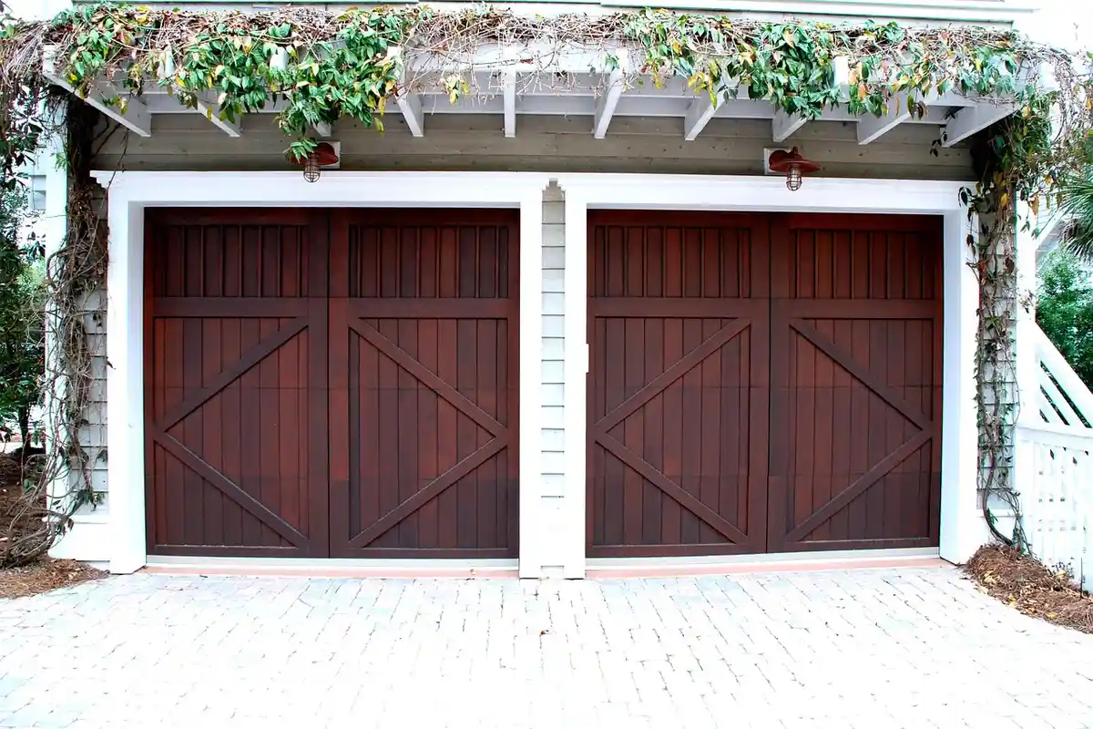 Two-car garage with brown wooden doors and white trim, ivy growing along the top beam.