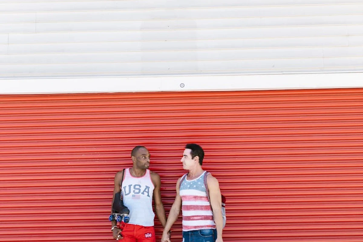 Two men stand in front of a red garage door, discussing garage door operation.