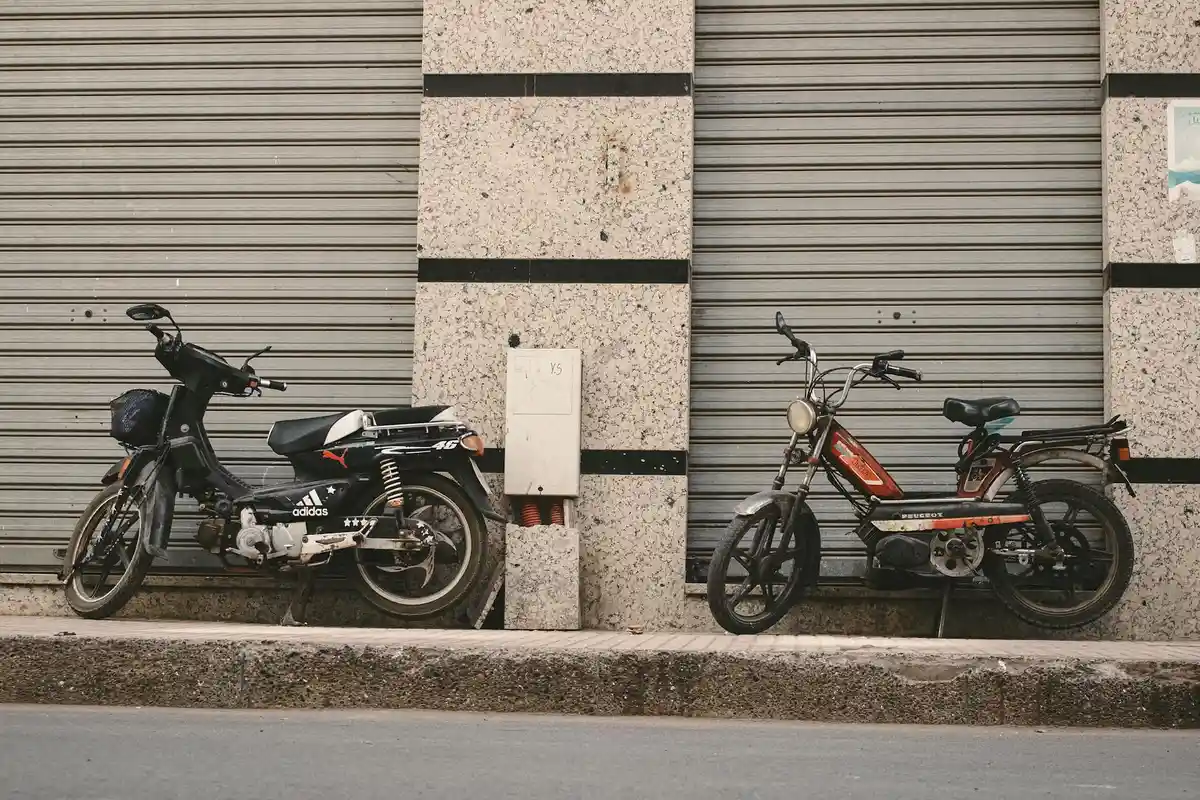 Two motorcycles parked along a city sidewalk in front of a building with closed metal shutters.