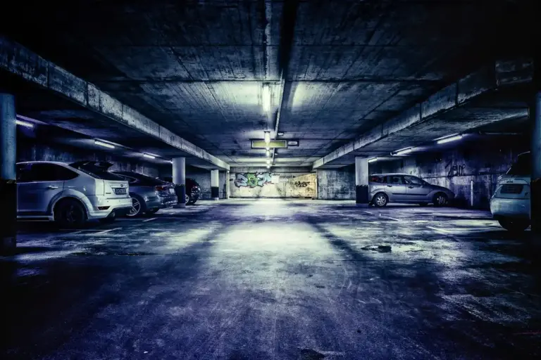 Dimly lit underground parking garage with cars parked along the sides.