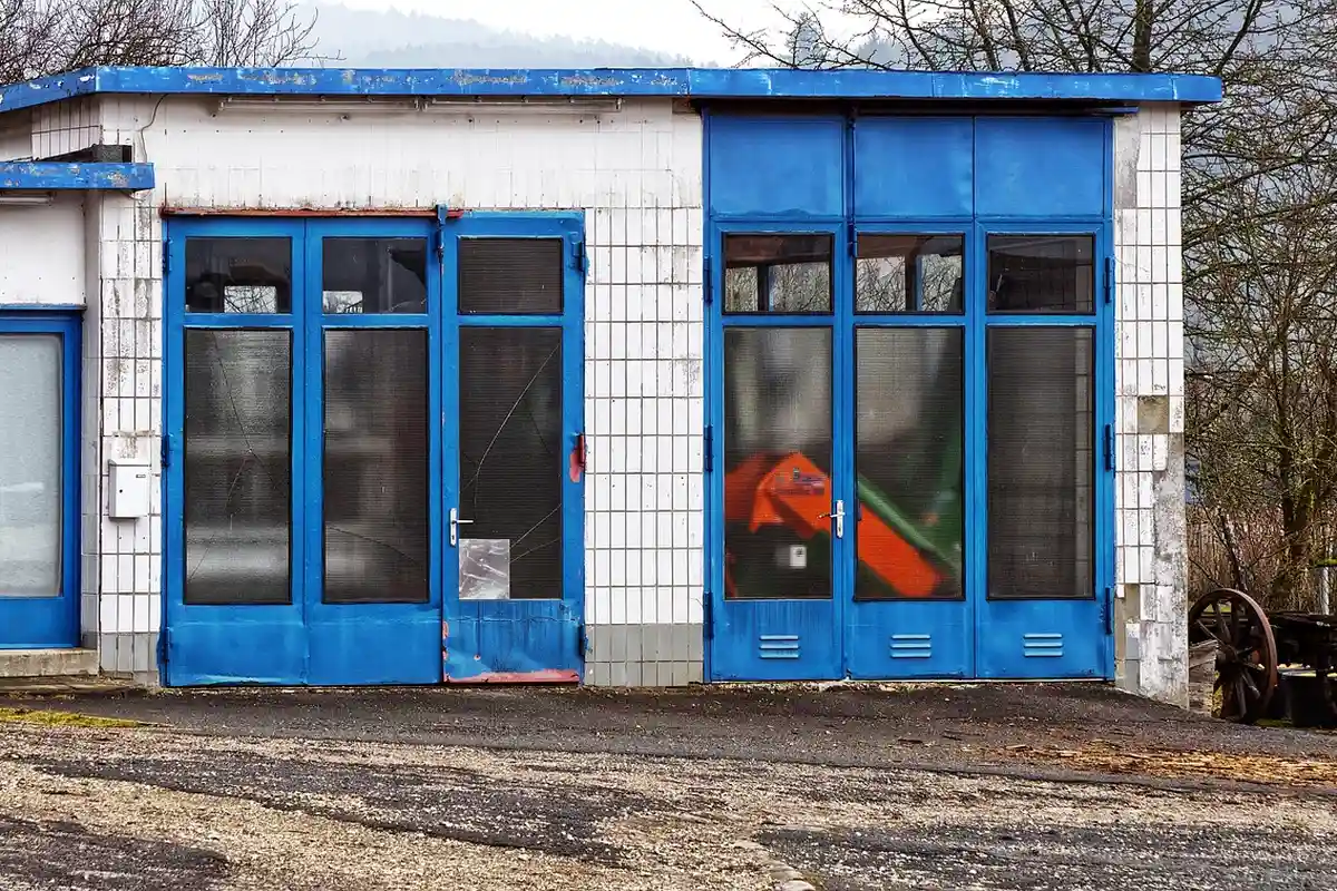 Exterior view of a small blue garage workshop with blue doors and white tiled walls