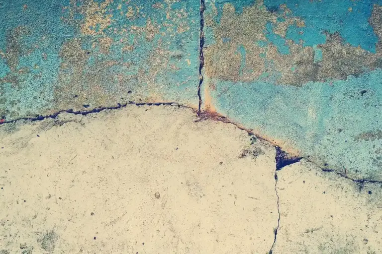 Close-up of a cracked concrete floor with peeling teal paint, illustrating durability and installation concerns for epoxy coatings.