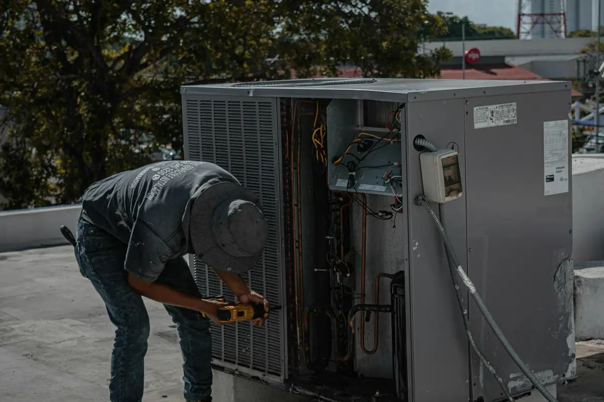 Technician servicing an outdoor air conditioning condenser on a garage rooftop.