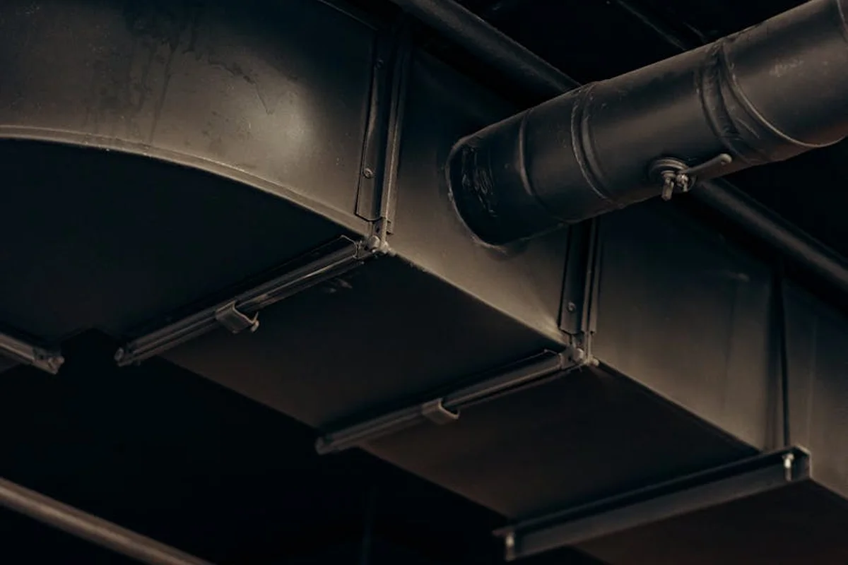 Metal ducting and pipes mounted to a dark garage ceiling.