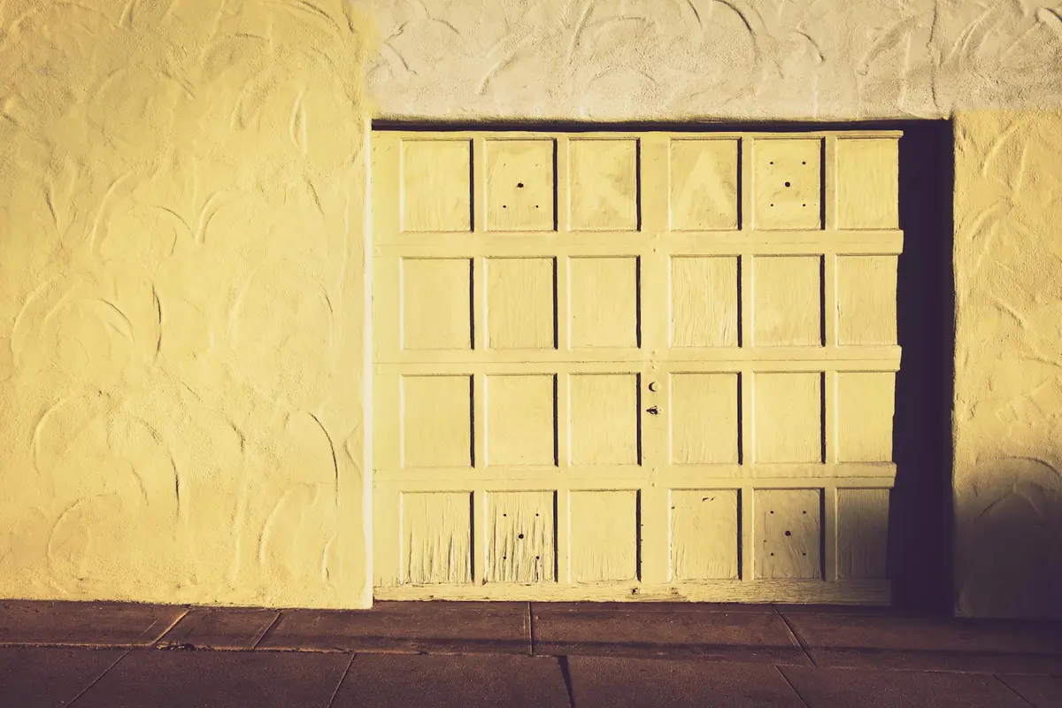 Exterior shot of a white, paneled garage door set into a textured stucco wall, illuminated by warm light