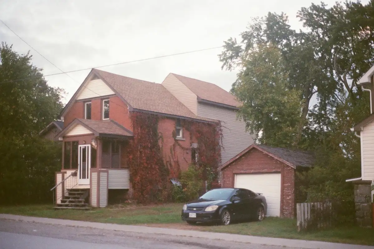 Front view of a suburban house with an attached garage; a black car is parked in the driveway, with ivy climbing part of the brick wall.