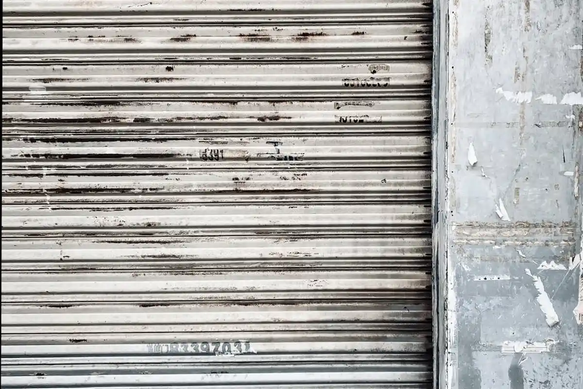 Weathered gray metal garage door with horizontal slats and a concrete wall edge.